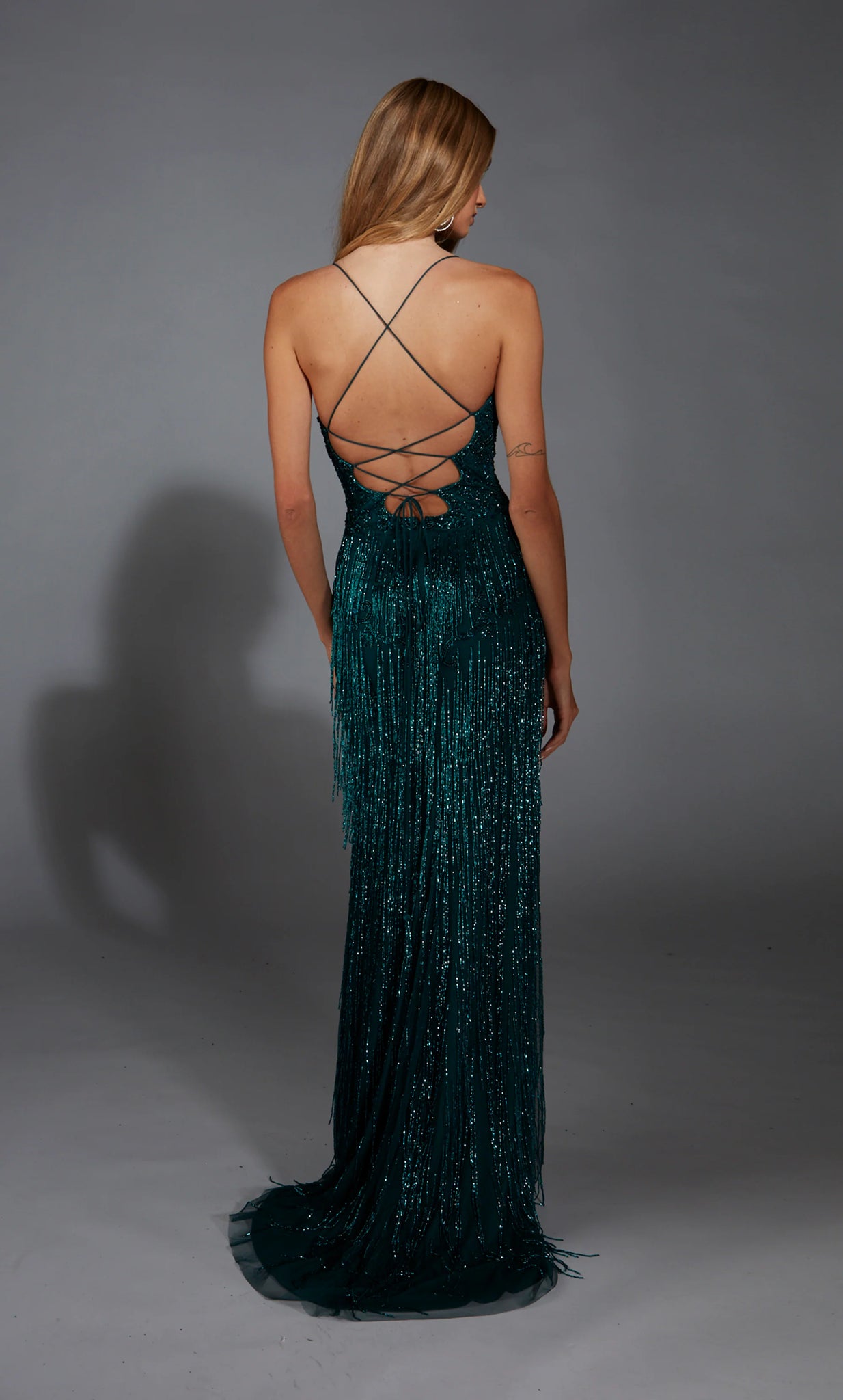 Amp up the drama in this glamorous long dress by Alyce Paris, style 61788. Showcasing a fitted silhouette with a modest v neckline that has delicate straps that lead to a sexy open back. This ensemble is fully adorned with glistening sequins and dazzling beadwork, the perfect final touches is the fringe detail in the skirt and the thigh high slit.