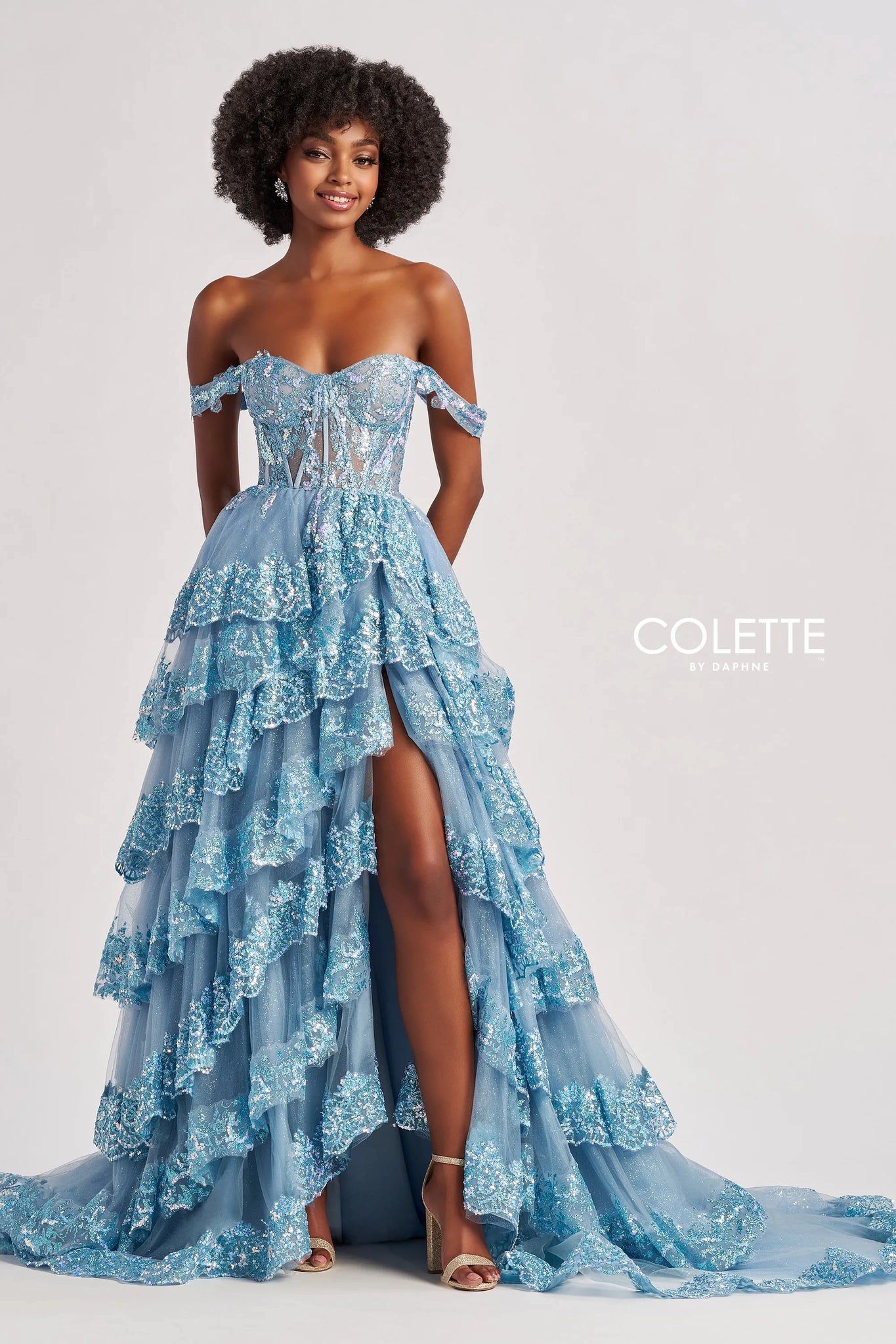 Make a glamorous entrance at your next special event in this stunning A line gown by Colette style CL8690. Showing an off the shoulder neckline adorning the fitted flattering corset bodice. A line skirt is adorned with a multi layered effect and beautiful thigh high slit and a stunning long sweep train.