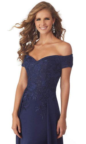 This stretch crepe evening gown presents in an off-shoulder neckline with a form-fitting bodice ornate with beaded lace appliques. The skirt runs in full length and is complemented with an overskirt and a train finish. Zip-up the back.  ONLY 1 IN STOCK  DISCONTINUED STYLE
