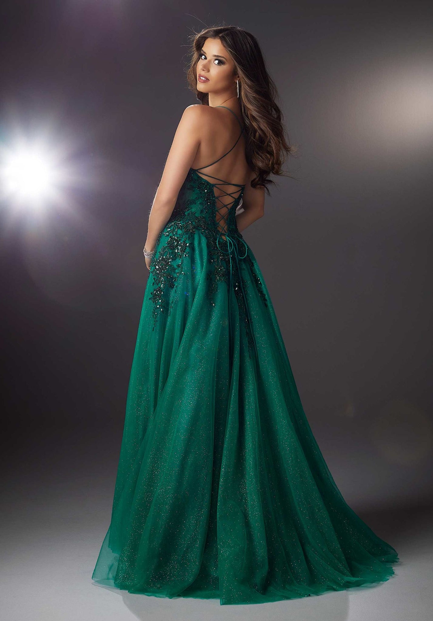 Elegant A-line prom features a delicate scoop neckline on a boned, corset bodice designed with stunning beaded lace appliqués that cascade down to the shimmering sparkle net skirt. Dainty spaghetti straps crisscross in the back leading to an open, lace-up corset back.