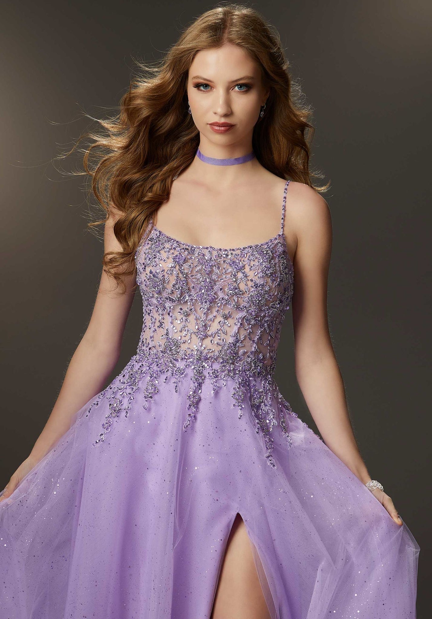 Gorgeous prom dress features a sheer embroidered bodice encrusted in rhinestone and crystal beading that meets a delicate glitter tulle skirt that floats off the body. A soft scoop neckline, delicately beaded straps, and a sultry skirt slit finish off the gown.