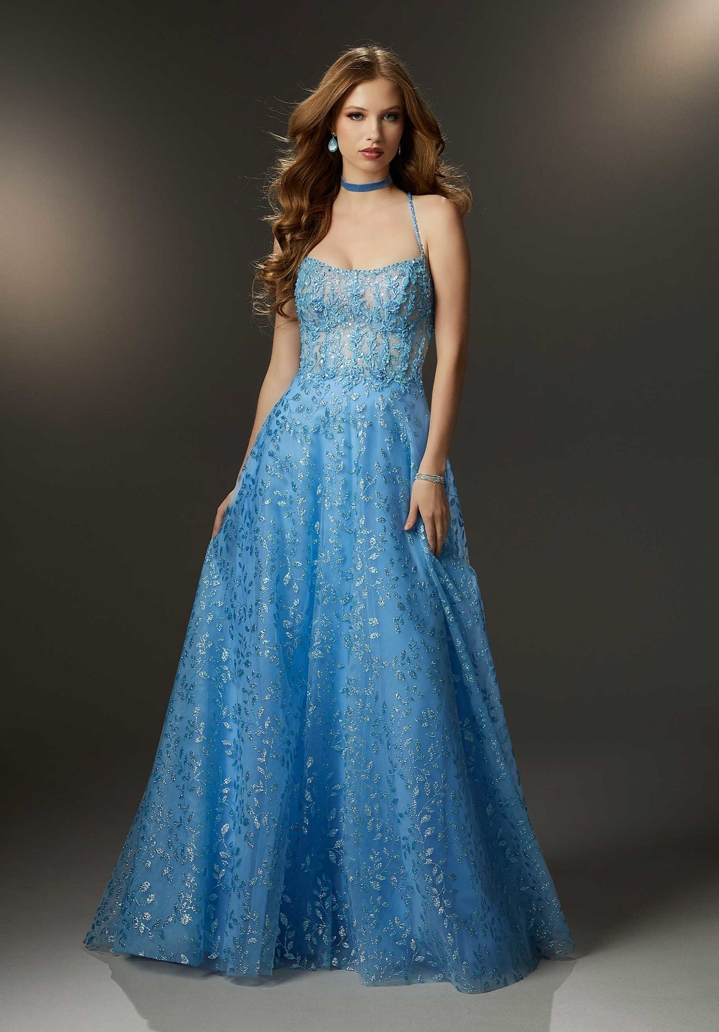 This lovely A-line prom dress has a sheer scoop neckline on a corset bodice with a softly flowing skirt all adorned in sparkling crystal beaded embroidery on botanical patterned glitter net. The delicate beaded straps crisscross in the back to meet up with a lace-up corset detail.